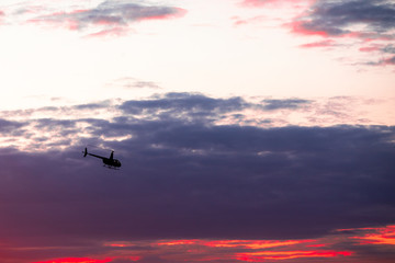 The helicopter in the astonishingly beautiful evening sky at sundown, rescue mission; aerial vehicle concept.