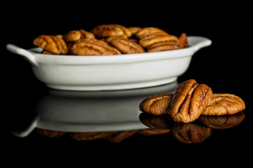 Lot of whole dry brown pecan nut in white oval ceramic bowl isolated on black glass