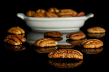 Lot of whole dry brown pecan nut in white oval ceramic bowl isolated on black glass