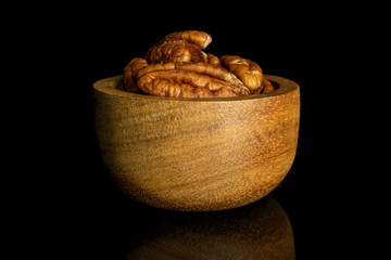 Lot of whole dry brown pecan nut in tiny wooden bowl isolated on black glass