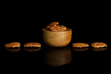 Lot of whole dry brown pecan nut in tiny wooden bowl isolated on black glass