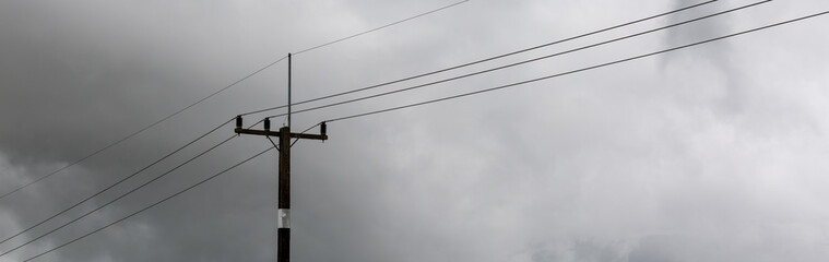 Electricity pole and high voltage power lines on the road with cloud and overcast sky