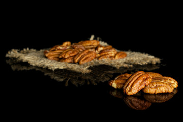 Lot of whole dry brown pecan nut on natural sackcloth isolated on black glass