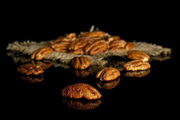 Lot of whole dry brown pecan nut on natural sackcloth isolated on black glass