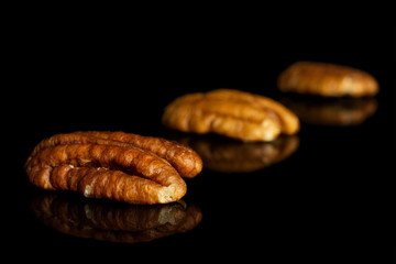 Group of three whole dry brown pecan nut isolated on black glass