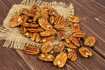 Lot of whole dry brown pecan nut on natural sackcloth on brown wood