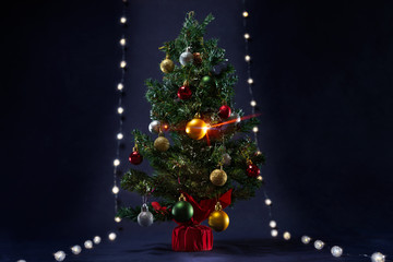 There is xmas tree with different colors ball between the glowing lights like runway.  It is on the black background. Merry Christmas. Happy New Year 2020. 