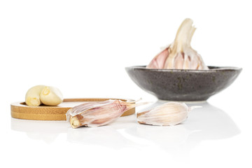 Group of one whole four pieces of aromatic white garlic on round bamboo coaster on glazed bowl isolated on white background