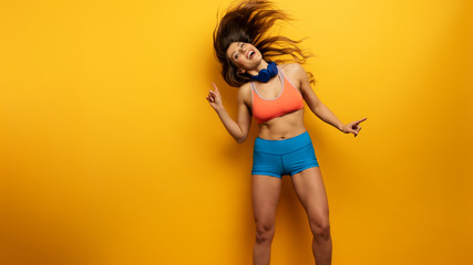 Fitness girl listens to music with headset. Joyful and happy expression on yellow background