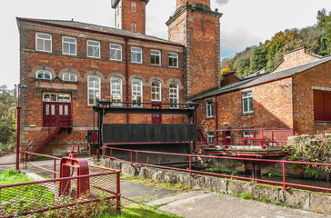 Old brick red factory with red metal railings and lots of windows near river