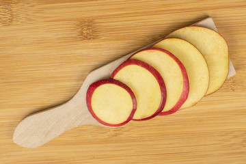 Group of five slices of fresh apple red delicious on wooden cutting board flatlay on light wood