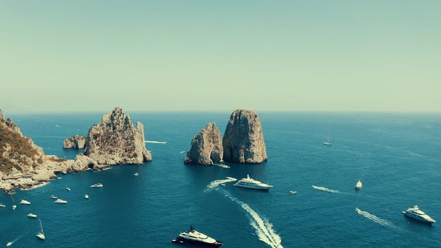 Aerial shot of the sea in front of the island of Capri, Italy, with a slow camera movement backwards, over the many ships berthed near the coast.