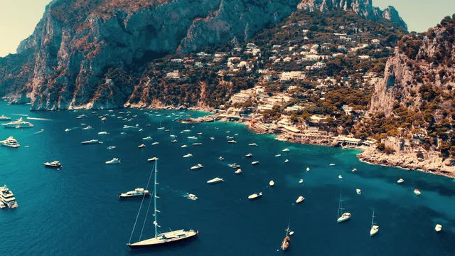 Aerial shot of the island of Capri, Italy, with a slow camera tilt over the luxury boats berthed and the coast, full of hotels and houses.