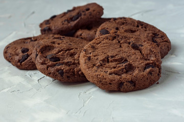 Scattered chocolate round cookies with pieces of chocolate on a light gray background. Concept for a delicious snack. Sweet dessert Rustic wooden background. Selective focus. Close up.