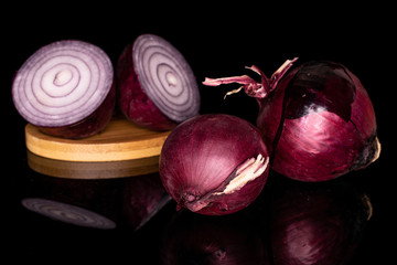 Group of two whole two halves of tasty onion red on round bamboo coaster isolated on black glass