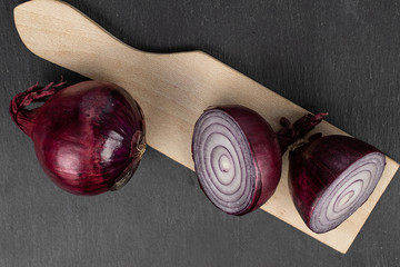 Group of one whole two halves of tasty onion red on wooden cutting board flatlay on grey stone