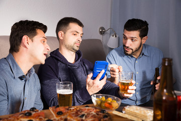 friends looking at phone while drinking beer