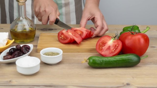 Girl cuts a red tomato for salad. Woman's hands preparing and cooking a Greek salad. Vegetarian cuisine. Healthy food. Greek salad recipe execution. Fresh vegetables and olive oil for salad.