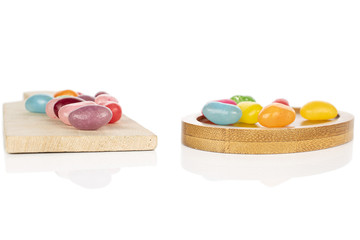 Lot of whole jelly bean candy on wooden cutting board on round bamboo coaster isolated on white background