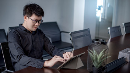 Young Asian businessman using digital tablet in office meeting room. Male entrepreneur reading news on social media app. Online marketing and Big data technology for E-commerce business. 