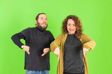 Beautiful young couple over green isolated background pointing, funny and crazy expression.