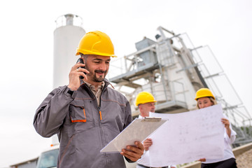 Civil engineer and colleagues on site, wearing safety helmet, checking project status