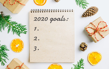 2020 goals plans dreams. New Year concept writing in notebook. Eco style. Gift box, thuja branches, dried oranges, cones on white background. Flat lay. Top view