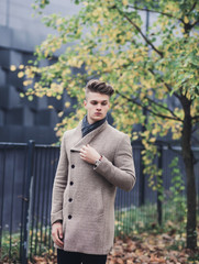 Fashion model man in coat posing in autumn park