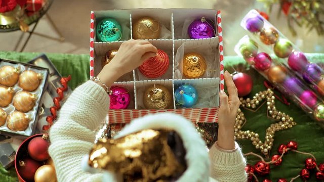 Holiday season. Upper view of young housewife in sparkle gold sequin santa hat sitting on divan in the modern living room at Christmas took out Christmas ornaments to decorate house. PRORes 422 codec.