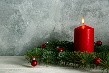 Bunch of red candles burning on wood textured table with traditional christmas pine decoration on grunged concrete background with a lot of copy space for text.