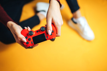 Young woman playing with two gamepads on yellow.