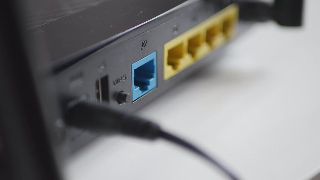 Man's Hand Unplugging Blue Internet Cable From Wireless Router.