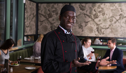 Obraz premium Smiling African American chef inviting to restaurant