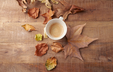 Mug of coffee and autumn leaves. Rustic wooden background. Top view. 