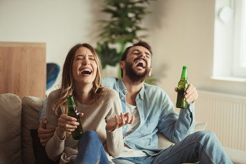 Happy couple having fun while drinking beer at home