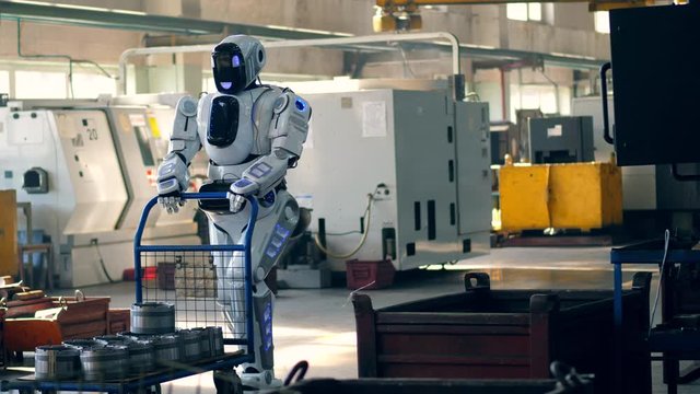 Working robot pulls a cart with metal boxes at a factory.