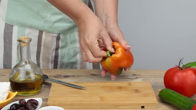 Girl cleaning a bell papper for salad. Woman's hands preparing and cooking a Greek salad. Vegetarian cuisine. Healthy food. Greek salad recipe execution. Fresh vegetables and olive oil for salad.