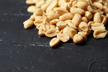 Roasted peeled peanuts closeup, salty beer snack scattered on black stone background