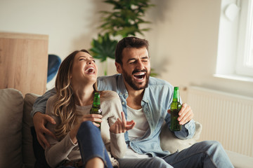 Happy couple having fun while drinking beer at home