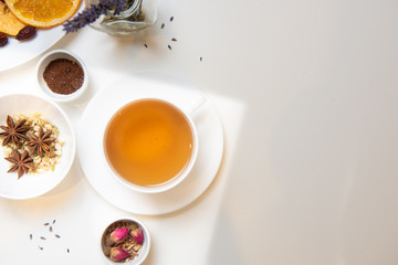 a white mug on a white table with herbal tea and herbal ingredients laid out on the table. Concept on the topic of herbal treatment for colds and flu in autumn. Top view