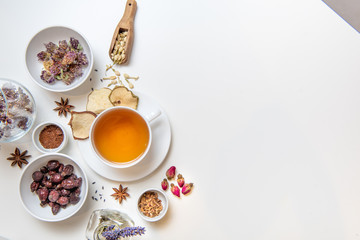 a white mug on a white table with herbal tea and herbal ingredients laid out on the table. Concept on the topic of herbal treatment for colds and flu in autumn. Top view