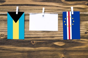 Hanging flags of Bahamas and Cape Verde attached to rope with clothes pins with copy space on white note paper on wooden background.Diplomatic relations between countries.