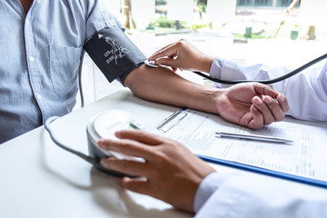 Doctor using stethoscope checking measuring arterial blood pressure on arm to a patient in the...