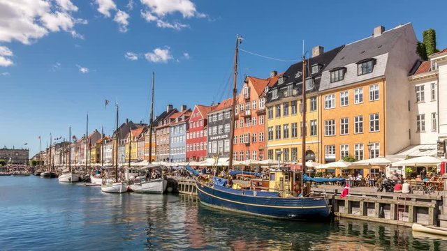 Time lapse video of Nyhavn canal (New Harbour), a 17th-century waterfront and entertainment district in Copenhagen, Denmark. Colorful houses and sailing boats. White clouds move across blue sk