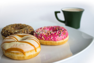 Fresh colorful donuts on a white plate and a Cup of coffee