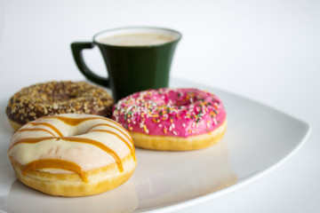 Fresh colorful donuts on a white plate and a Cup of coffee