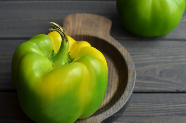 Big fresh organic green bell pepper in wooden plate on dark wooden table background, copy space