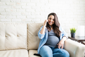 Obraz premium Pretty Pregnant Woman Sitting With Mobile Phone At Home