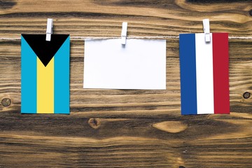 Hanging flags of Bahamas and Netherlands attached to rope with clothes pins with copy space on white note paper on wooden background.Diplomatic relations between countries.