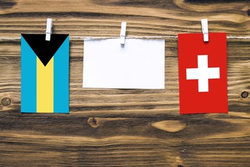 Hanging flags of Bahamas and Switzerland attached to rope with clothes pins with copy space on white note paper on wooden background.Diplomatic relations between countries.